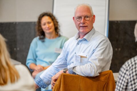 Aanwezige man bij event zit op stoel en draait zich om naar camera.